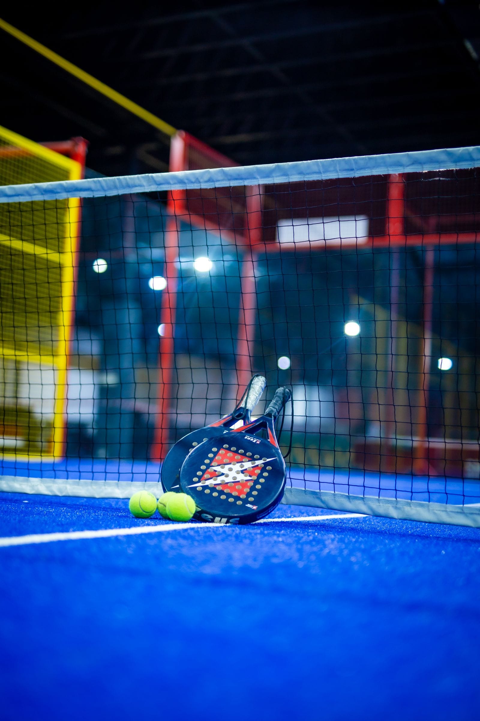 Two padel rackets and balls resting against the net on a blue court