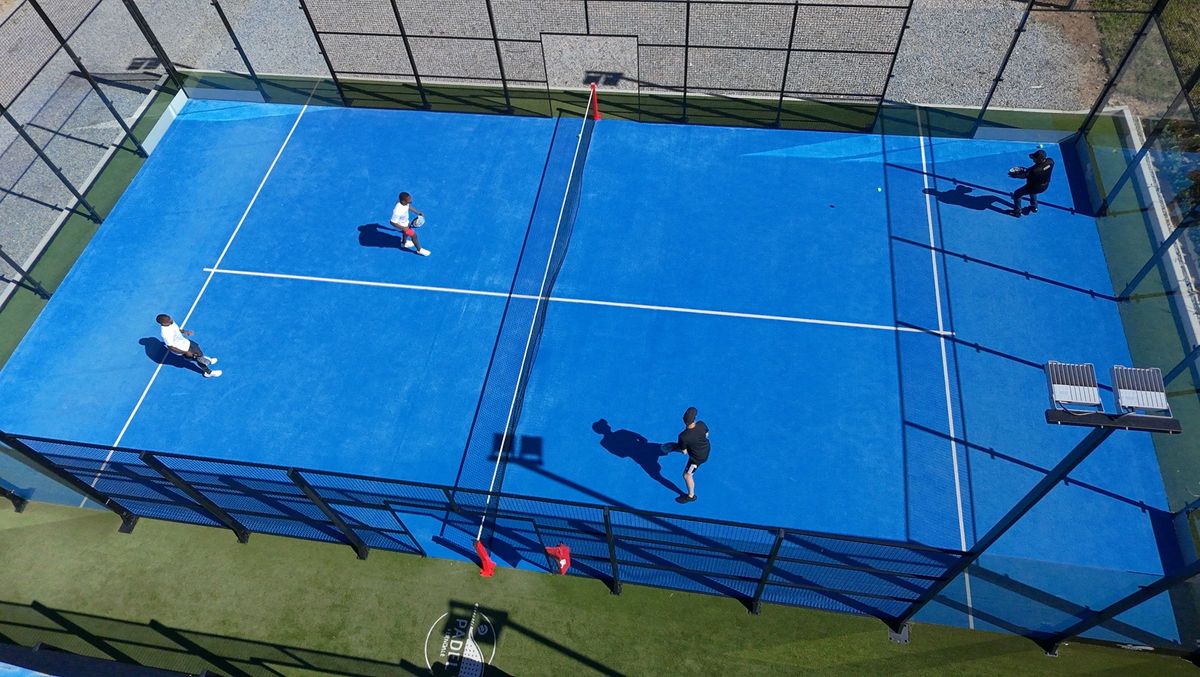 Four padel players competing in a doubles match on a blue outdoor court viewed from above