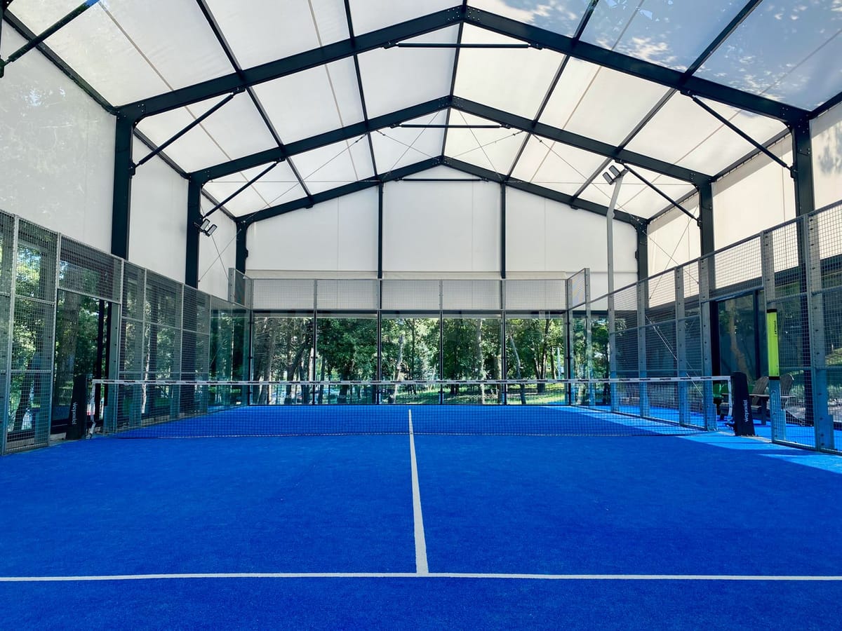 Empty covered padel court with blue turf and glass walls