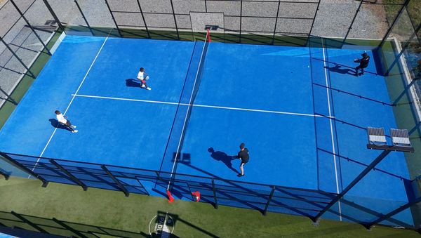 Four padel players competing in a doubles match on a blue outdoor court viewed from above