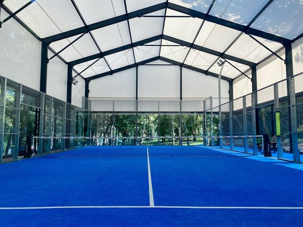 Empty covered padel court with blue turf and glass walls
